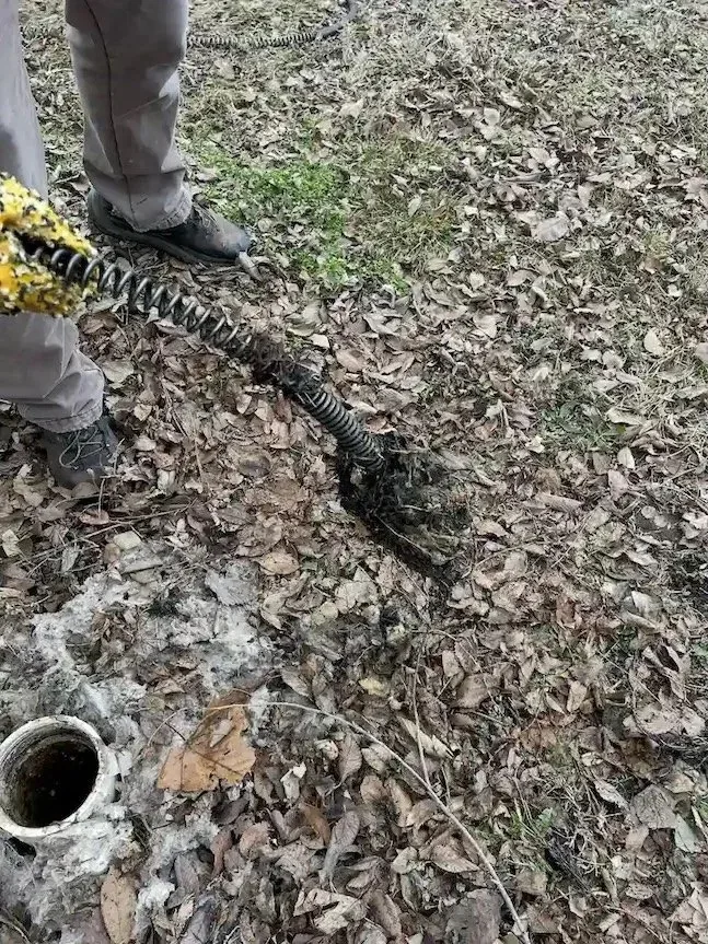 Technician pulling a mud-covered drain auger cable from an outdoor sewer cleanout